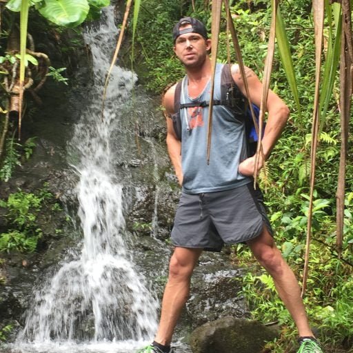 Matt Miller standing by a waterfall surrounded by lush tropical vegetation