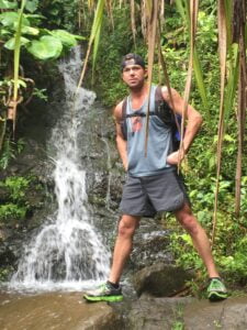 Matt Miller standing by a waterfall surrounded by lush tropical vegetation