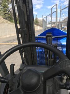 View from inside a forklift outdoors showing the steering wheel and parts of the lift