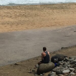 Sandy beach with a man sitting on a rock
