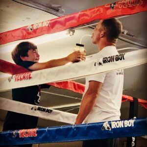 Matt Miller inside an MMA ring with a boy giving him a drink over the ropes
