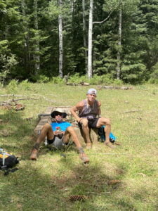 Matt Miller and an older man sitting in a meadow within a forest"