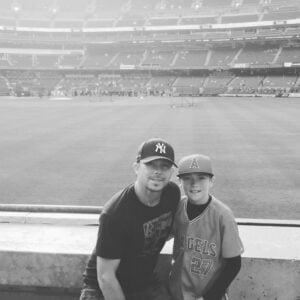 Black and white photo of Matt Miller with a boy at a baseball stadium, baseball field in the background