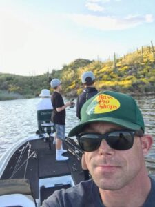 Matt Miller aboard a boat with boys fishing on a lake surrounded by hills covered in yellow and green shrubs and cacti