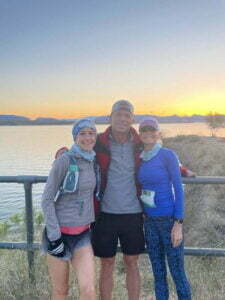 Matt Miller standing between two women with a scenic lake in the background, and distant land across the water