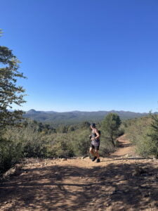 Matt Miller jogging towards the camera on a desert path, green shrubs on either side, and green hills in the distance under a clear blue sky