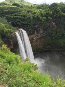 Spectacular waterfall cascading over a green-covered cliff into a serene pool below, photographed from a cliff adjacent to the waterfall